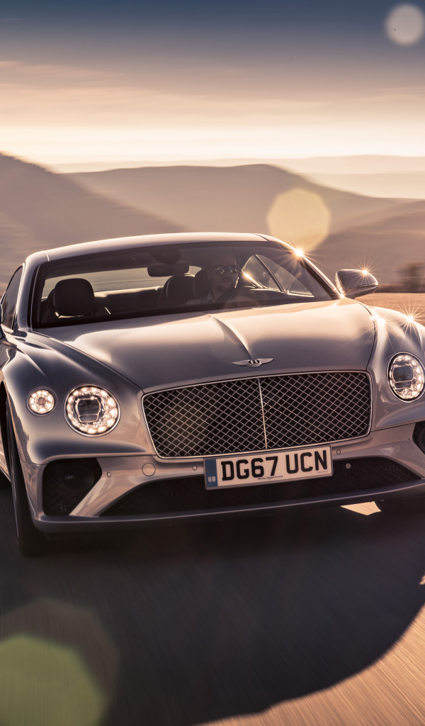 Серебристый автомобиль Bentley Continental GT 2018 года на трассе