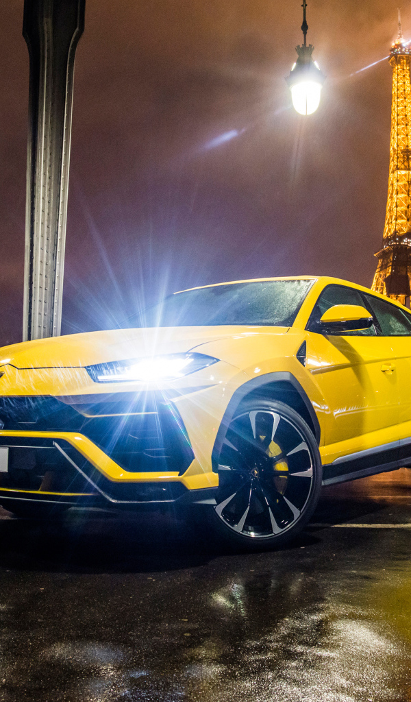 Желтый Lamborghini Urus, 2018 с включенными фарами на фоне Эйфелевой башни