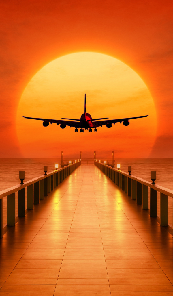 The airplane is landing at sunset over the ocean