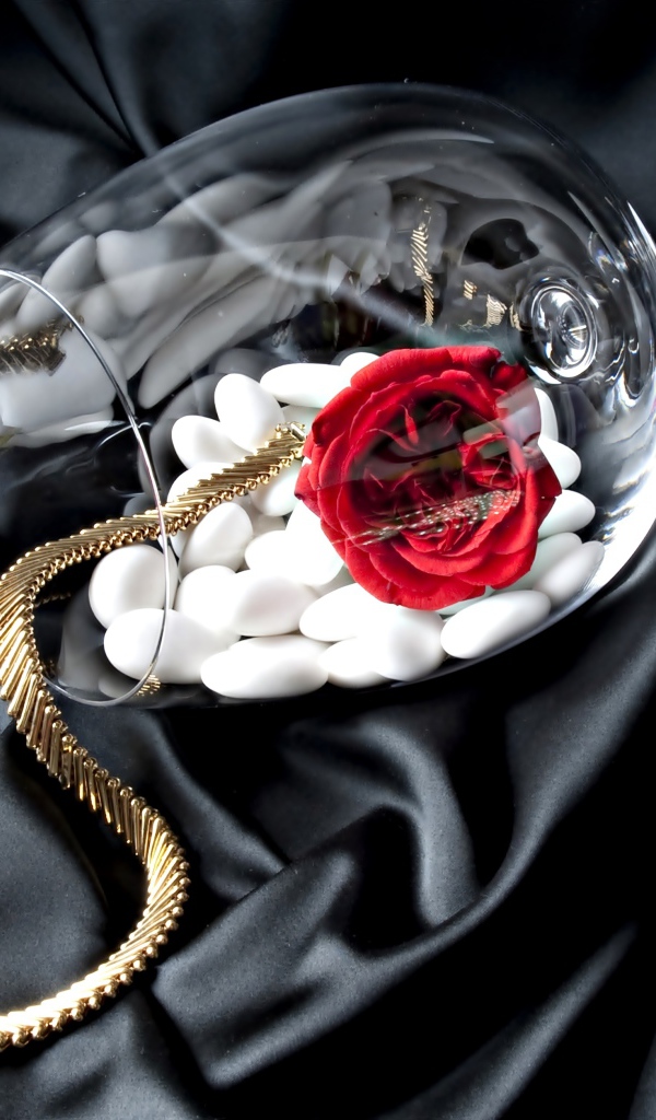 Бокал с золотой цепочкой, красной розой и белыми камнями на черном покрывале
