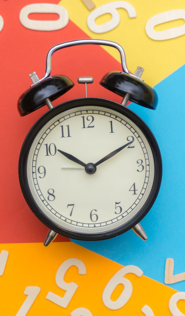 Будильник на разноцветном фоне с цифрами