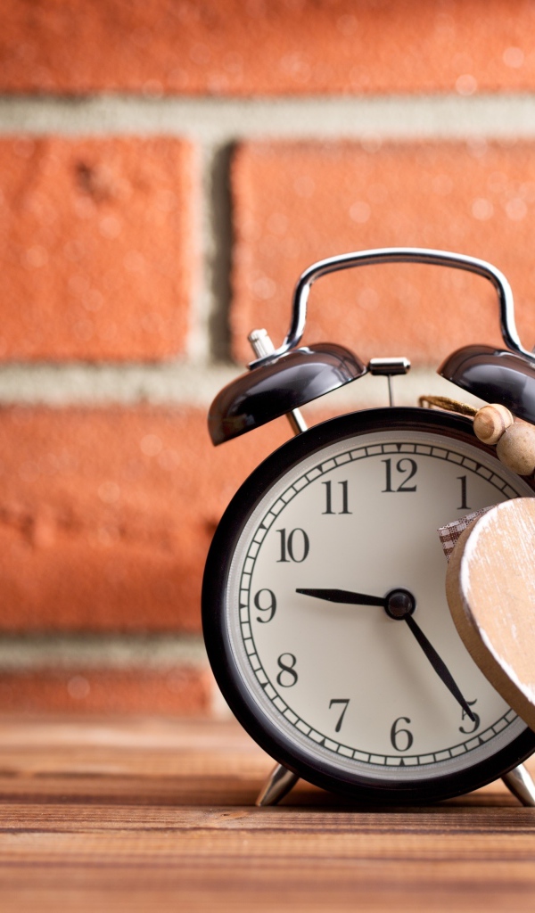 Будильник с деревянным сердцем стоит на фоне стены