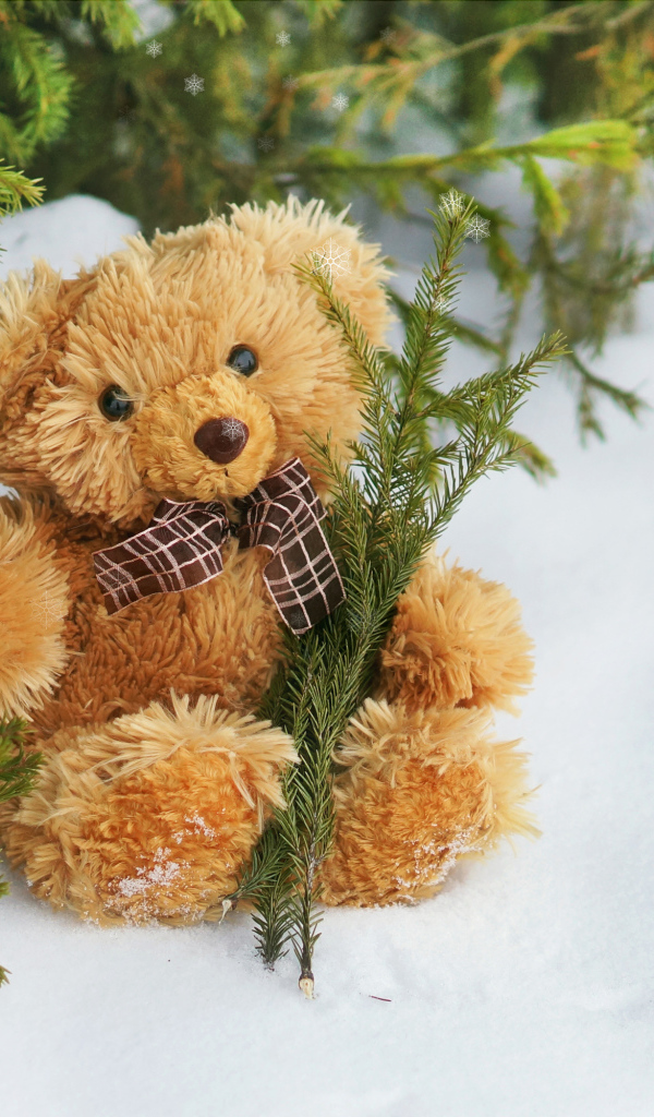 Медвежонок Тедди с веткой ели сидит на снегу