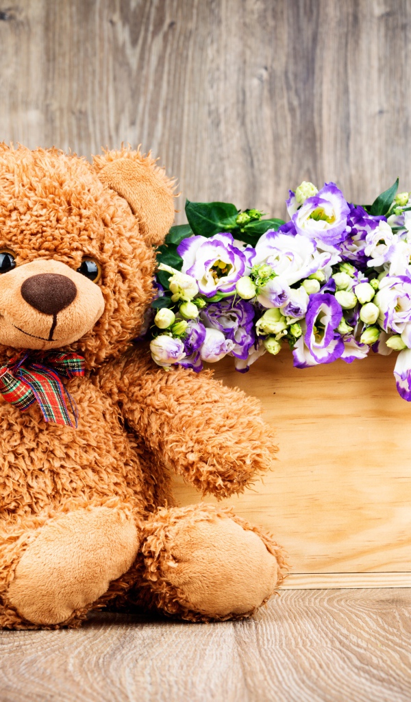 Плюшевый мишка с букетом цветов на деревянном фоне