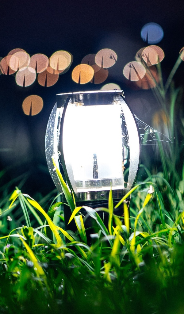 Включенный фонарь стоит в зеленой траве