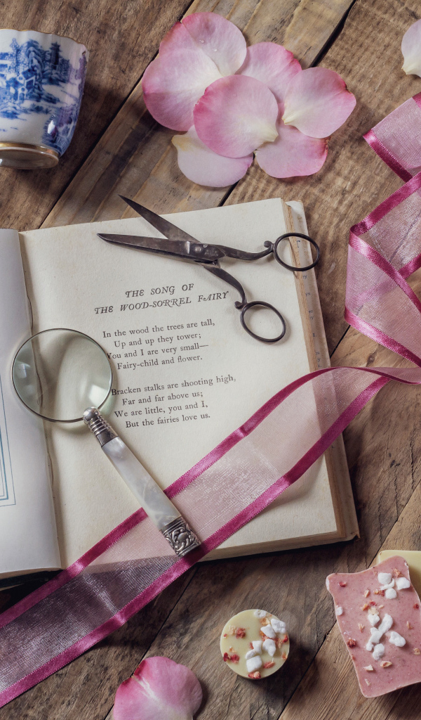 Старая книга на столе с увеличительным стеклом и искусственными цветами