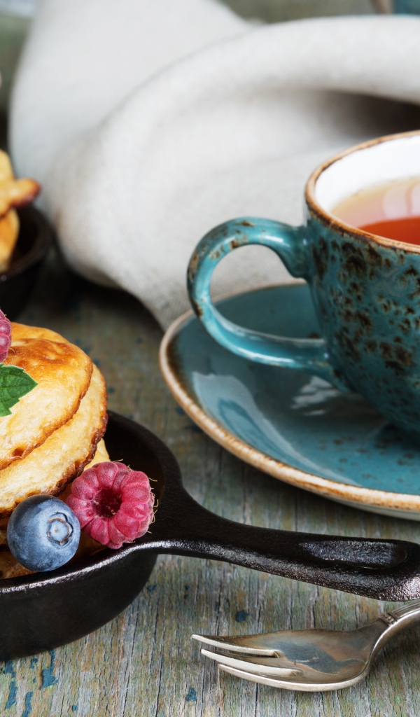 Чашка чаю с оладьями с ягодами на столе