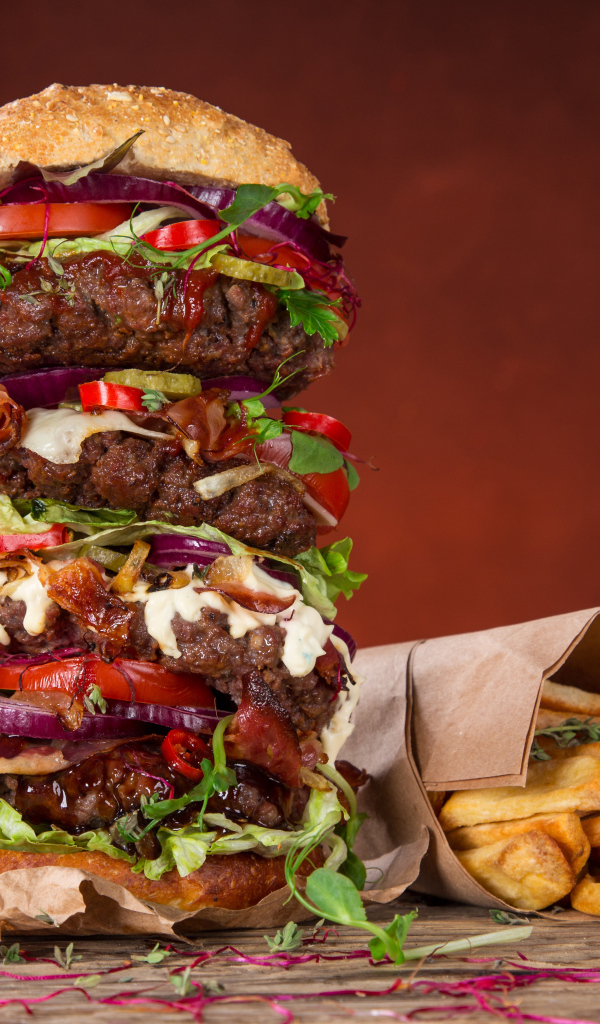 Огромный гамбургер на столе с картофелем фри и острым перцем