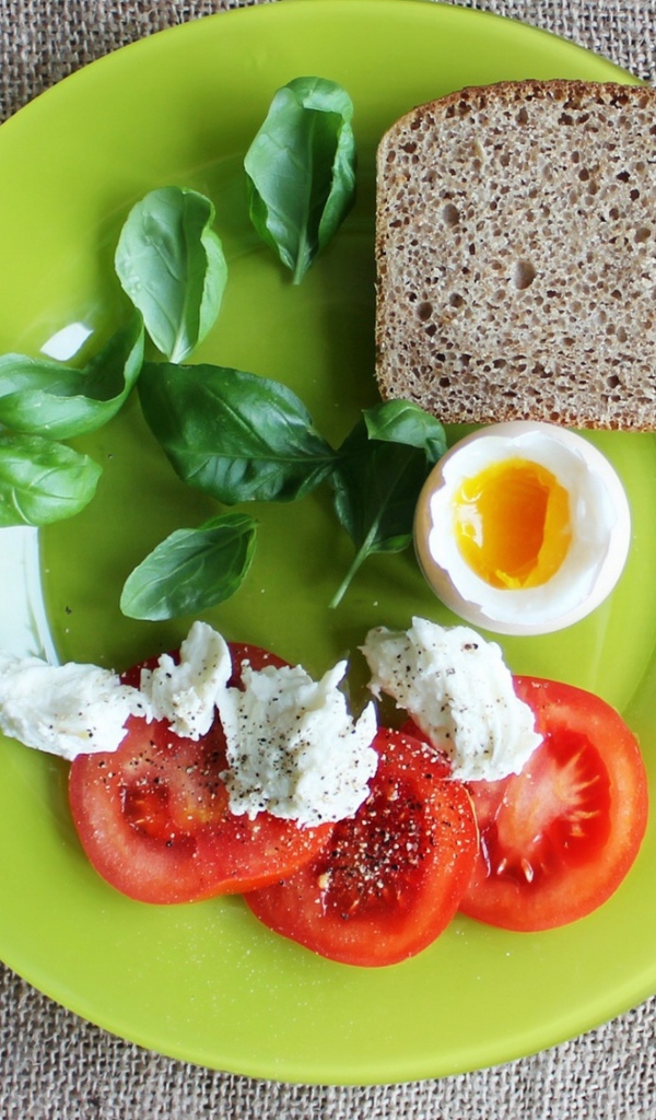 Легкий завтрак с помидорами, яйцом, кусочком хлеба и листьями базилика