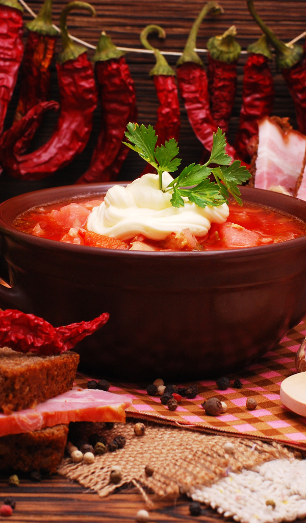 Тарелка борща на столе с красным острым перцем, чесноком, луком, зеленью и бужениной