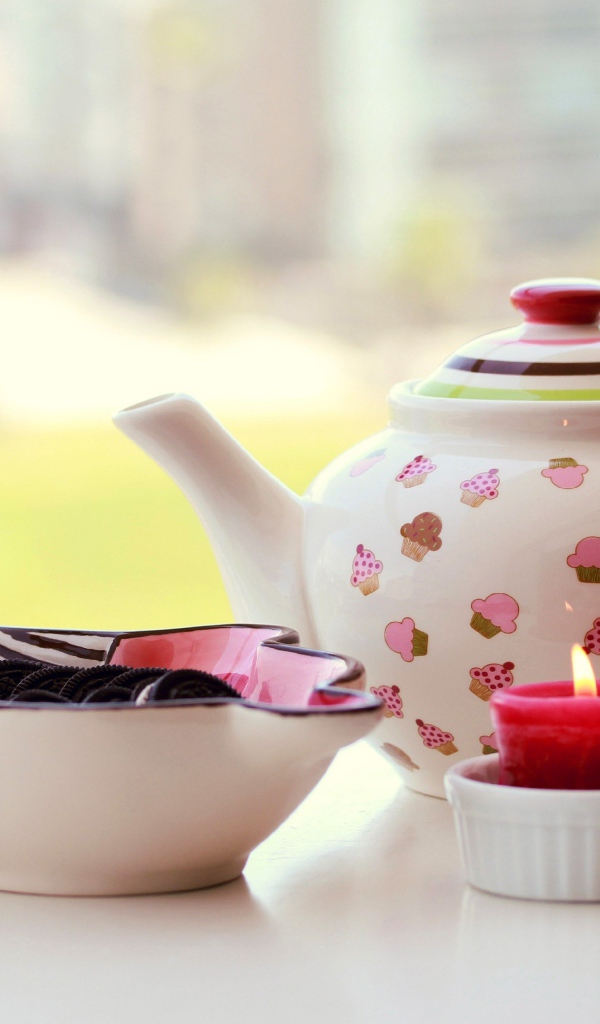 Чайник с печеньем орео и зажженной свечей на столе