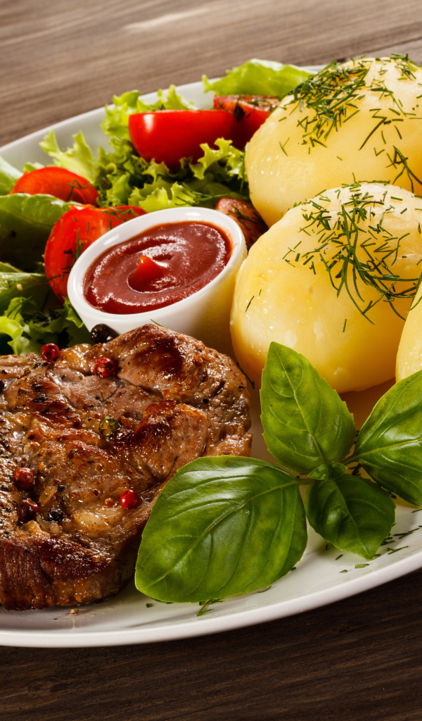 Вареный картофель с куском мяса и салатом на тарелке