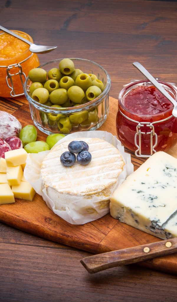 Сыр, грибы, маслины, колбаса, виноград и джем на разделочной доске 
