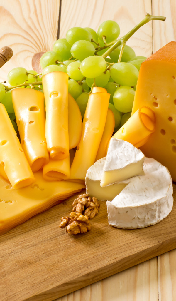 Сыр на столе с белым виноградом, медом и орехами 