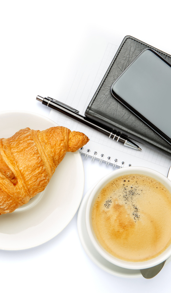 Чашка кофе, круассан, блонтон и смартфон на белом 