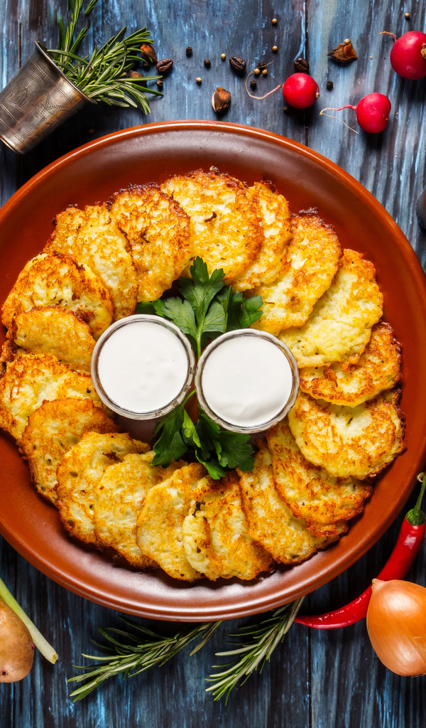 Драники с соусом на тарелке на столе с овощами