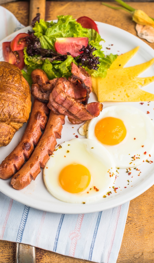 Яичница, салат, сосиски и круассан с соком на завтрак 