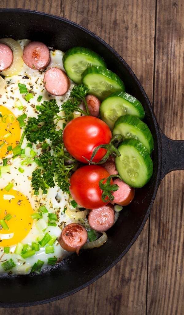 Яичница в сковороде с овощами и кусочками сосиски