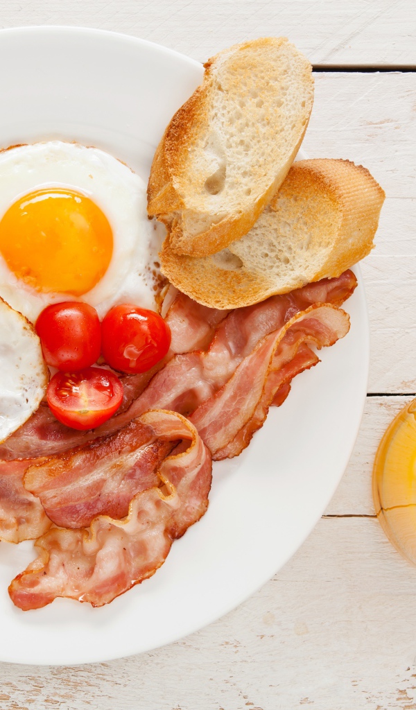 Яичница с беконом, гренками и помидорами на столе с соком 