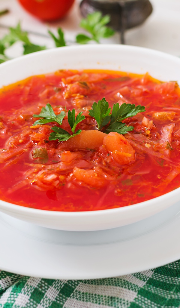 Горячий борщ с зеленью в белой тарелке на столе