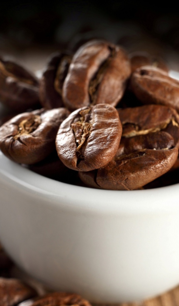 Много кофейных зерен в белой чашке на столе