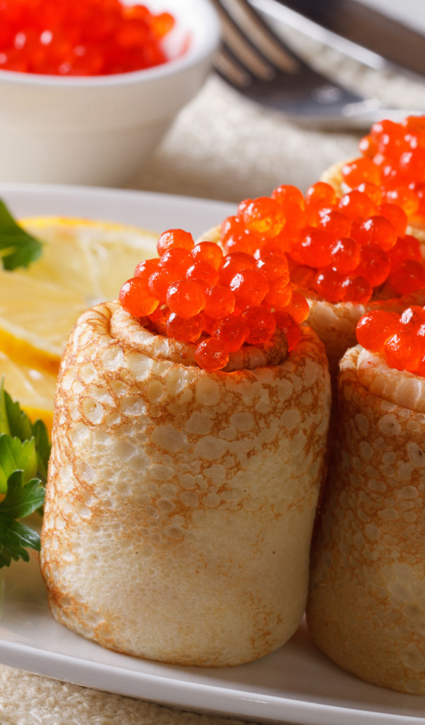 Блины с красной икрой на тарелке с лимонами и петрушкой