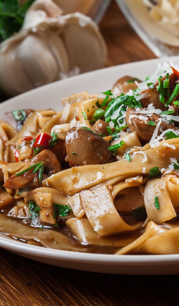 Паста с грибами, сыром и  зеленью на столе с чесноком 