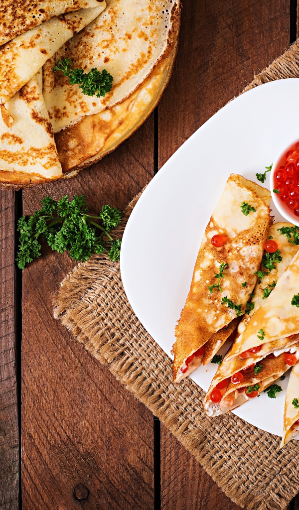 Рулетики из блинов на белой тарелке с красной икрой 