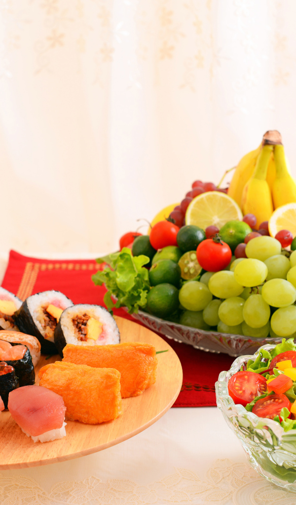 Роллы на столе с овощным салатом и фруктами 