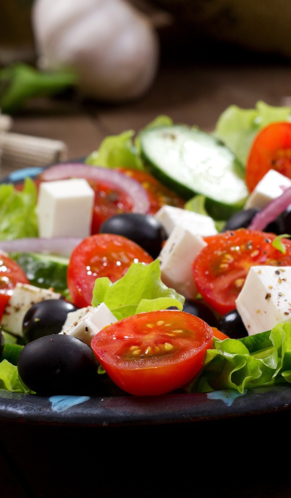 Салат с помидорами, огурцами, оливками, кусочками сыра и луком на листьях салата