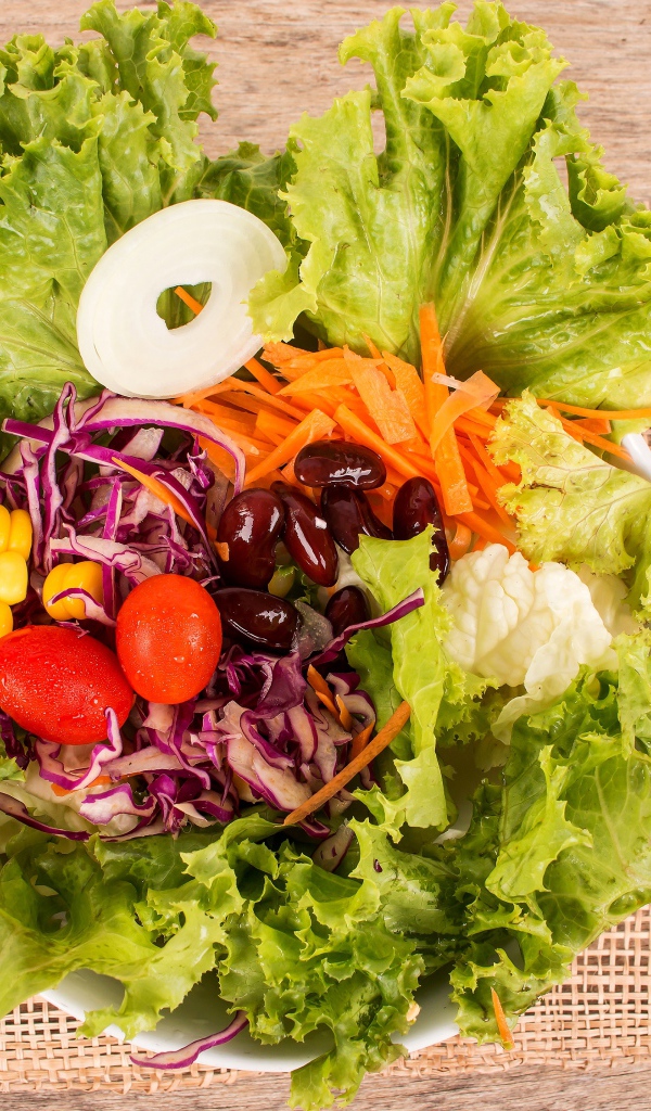 Салат с овощами и зелеными листьями салата в тарелке на столе со столовыми приборами