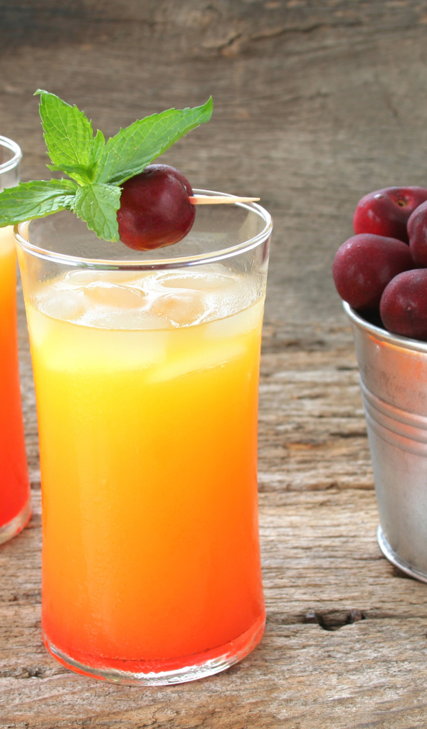 Два стакана напитка на столе с ведром с черешней