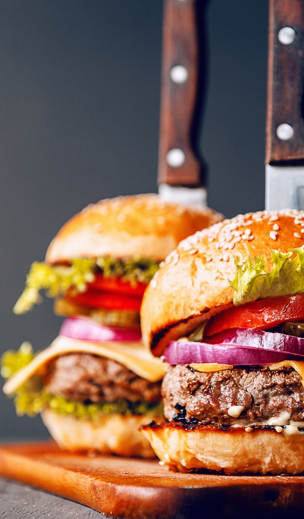 Два гамбургера с ножами на разделочной доске 