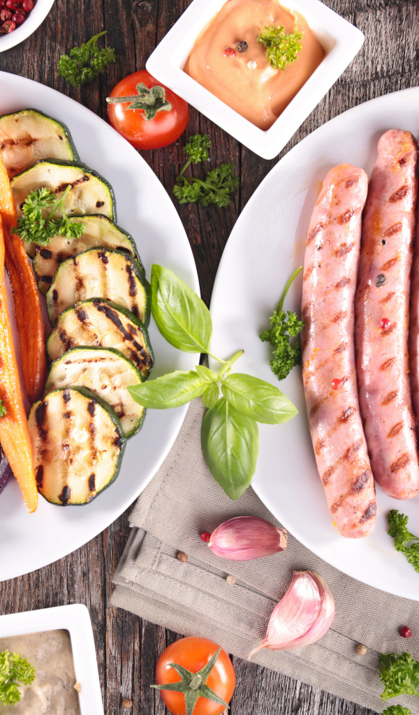 Овощи и сосиски гриль на столе с соусом