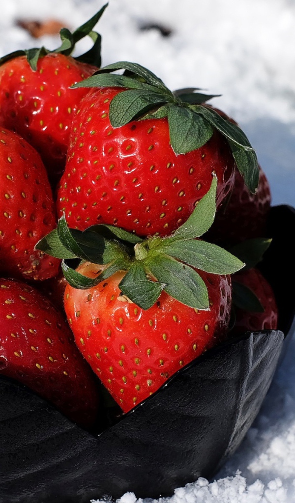 Тарелка со спелой красной клубникой стоит на белом снегу