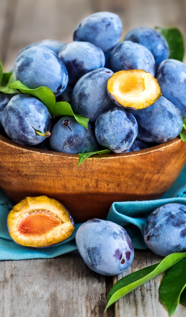 Синие сливы в деревянной миске с зеленой листвой
