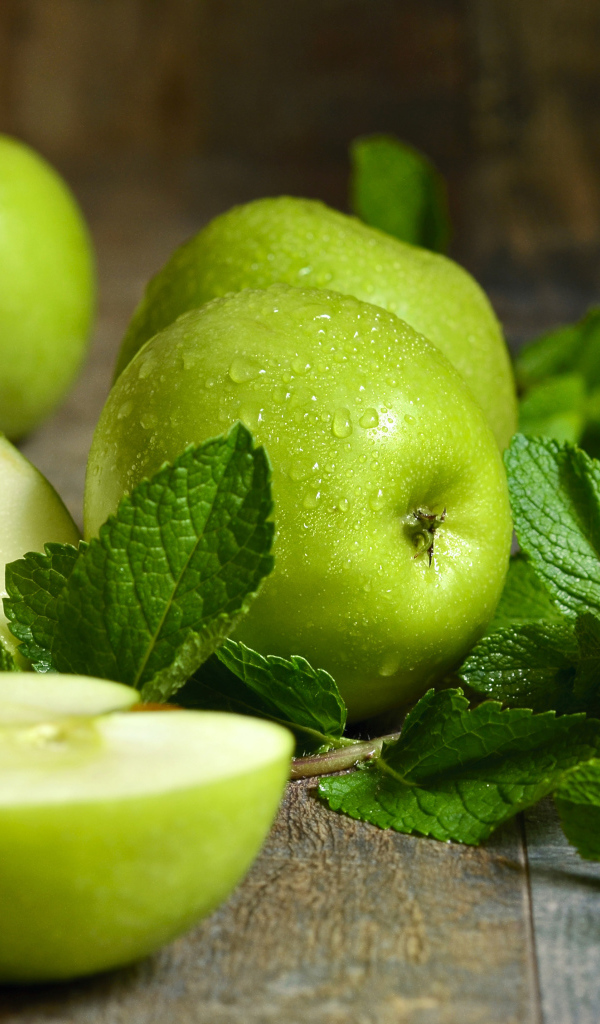 Зеленые яблоки в каплях воды на столе с мятой