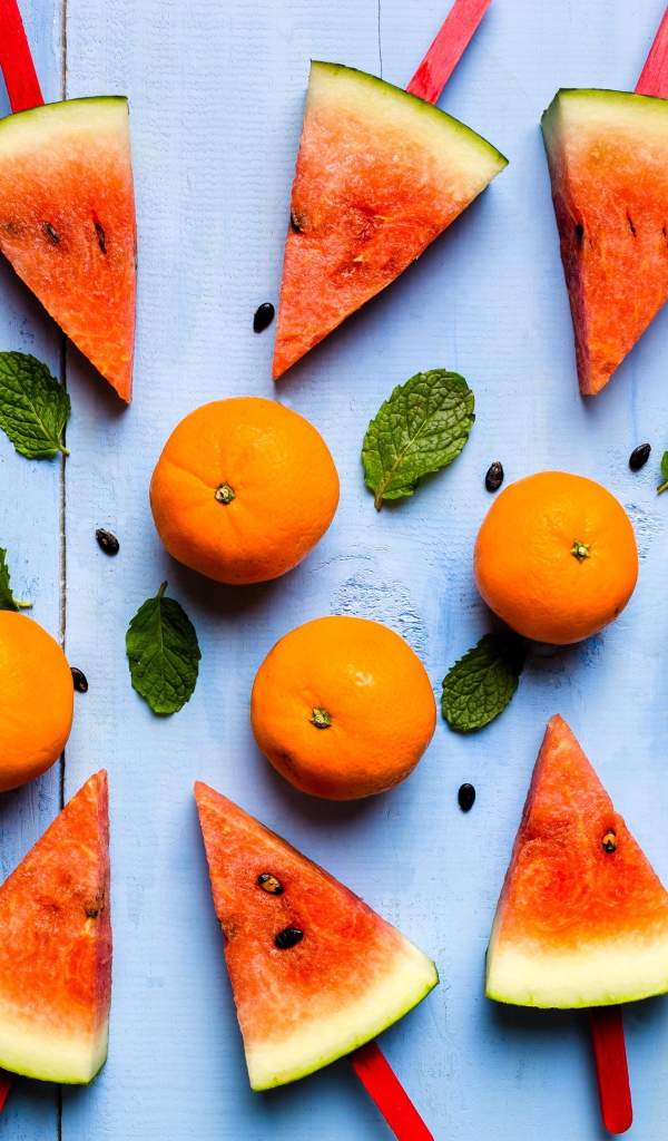 Кусочки арбуза на палочках на столе с мандаринами