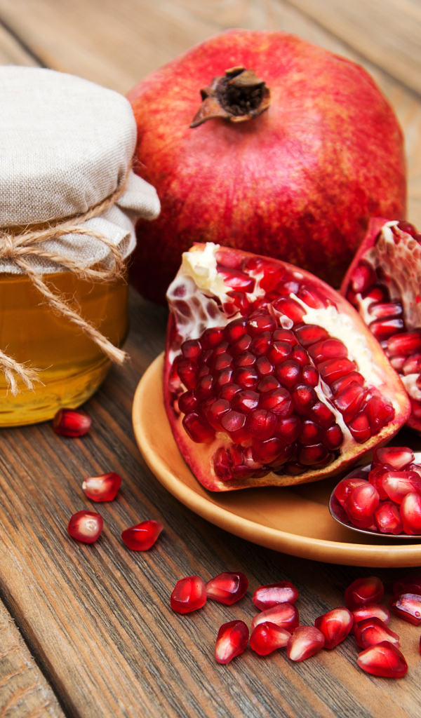 Гранат на деревянном столе с банкой меда