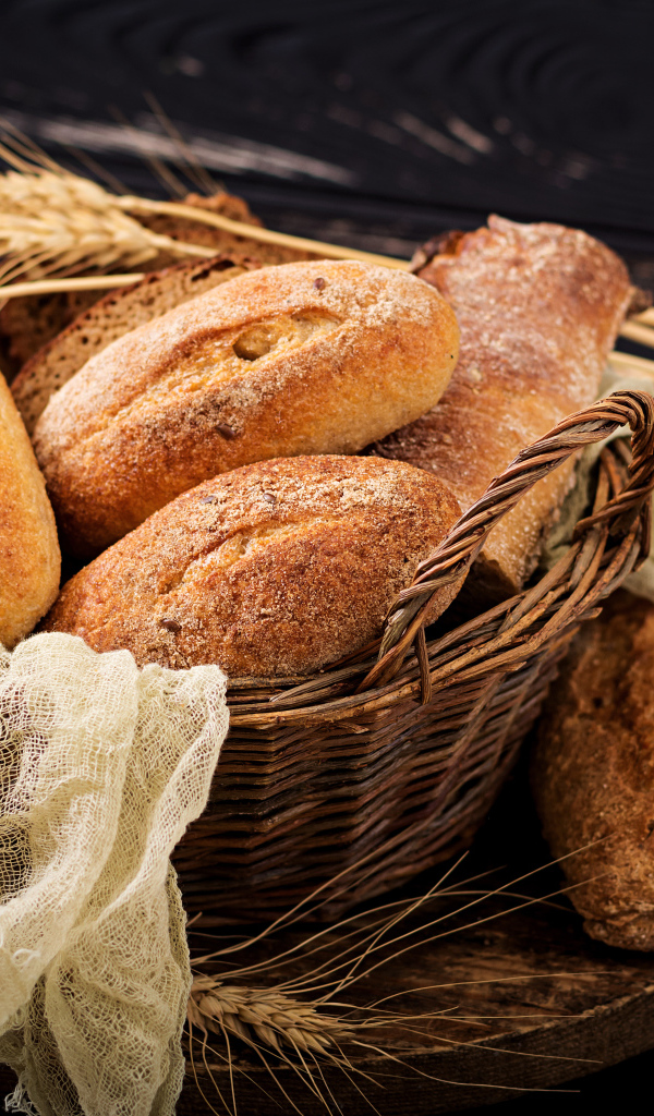 Свежая выпечка в корзине на столе с колосьями пшеницы