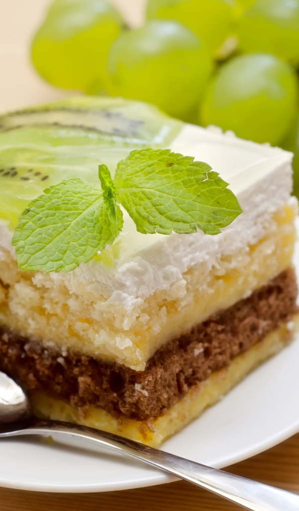 Кусок торта с киви и мятой на столе с виноградом