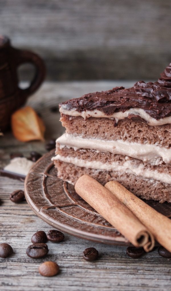 Кусок торта с корицей на столе с шоколадом и чашкой кофе