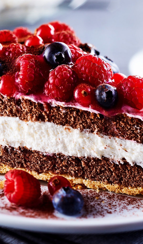 Аппетитный кусок торта на тарелке с ягодами малины, красной смородины и черники