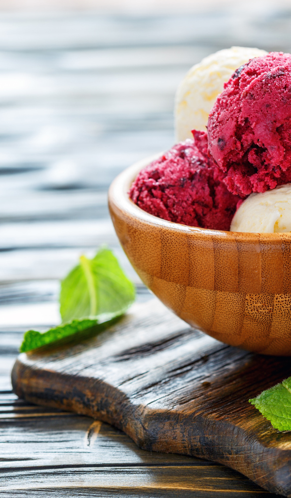 Шарики фруктового и ванильного мороженого в деревянной миске на столе