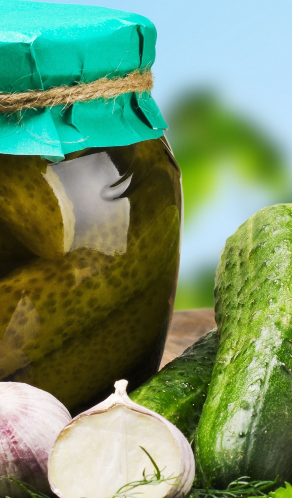 Консервированные огурцы в банке на столе со свежими огурцами и чесноком