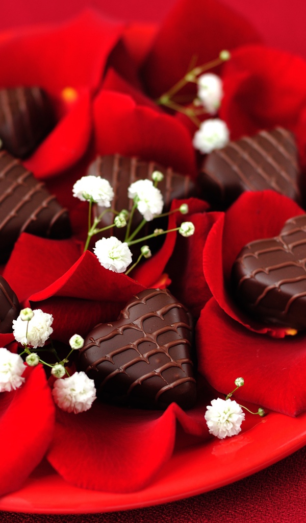 Шоколадные конфеты в форме сердца на тарелке с лепестками розы