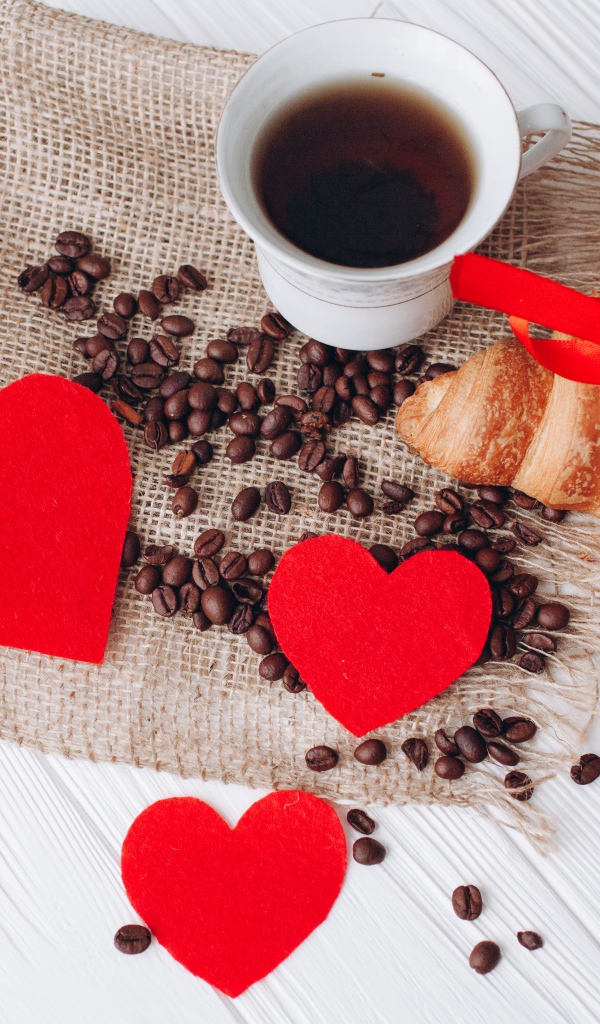 Круассан с чашкой кофе и кофейными зернами на столе с красными сердечками