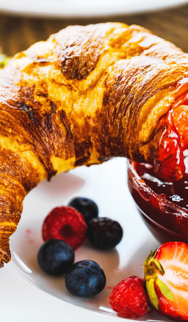 Круассан с джемом и ягодами на тарелке