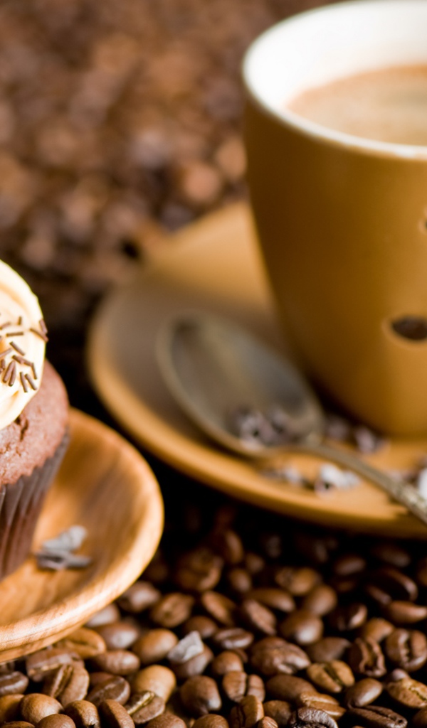 Кекс с кремом и чашкой кофе стоят на кофейных зернах 