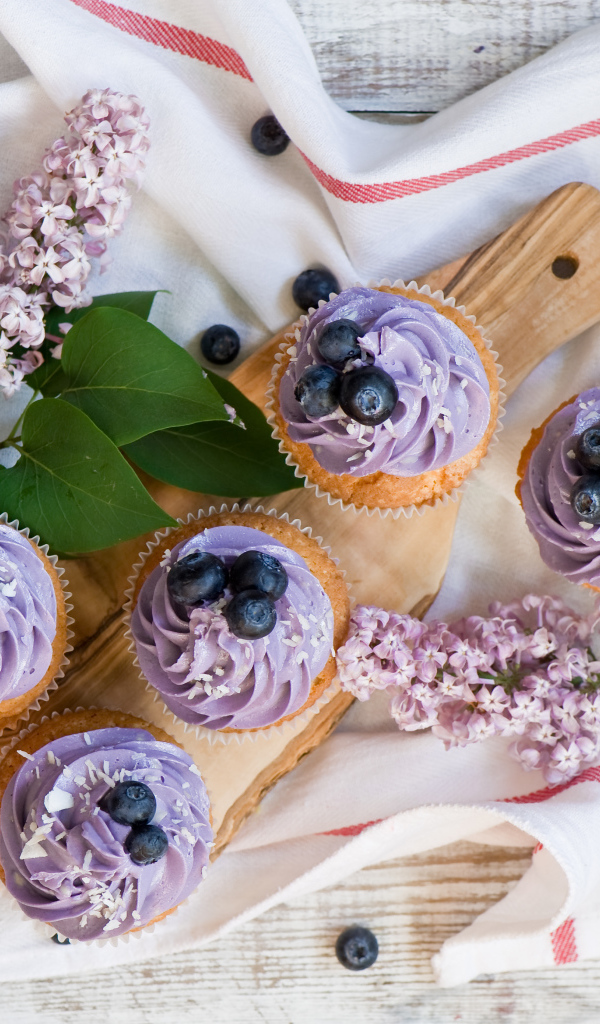 Кексы с кремом и ягодами черники на столе с ветками сирени 